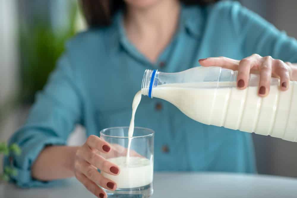 一个女人把牛奶从瓶子里倒到杯子里