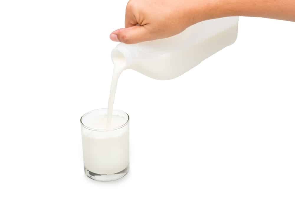 一手拿着装在塑料加仑里的新鲜牛奶，同时倒进杯子里